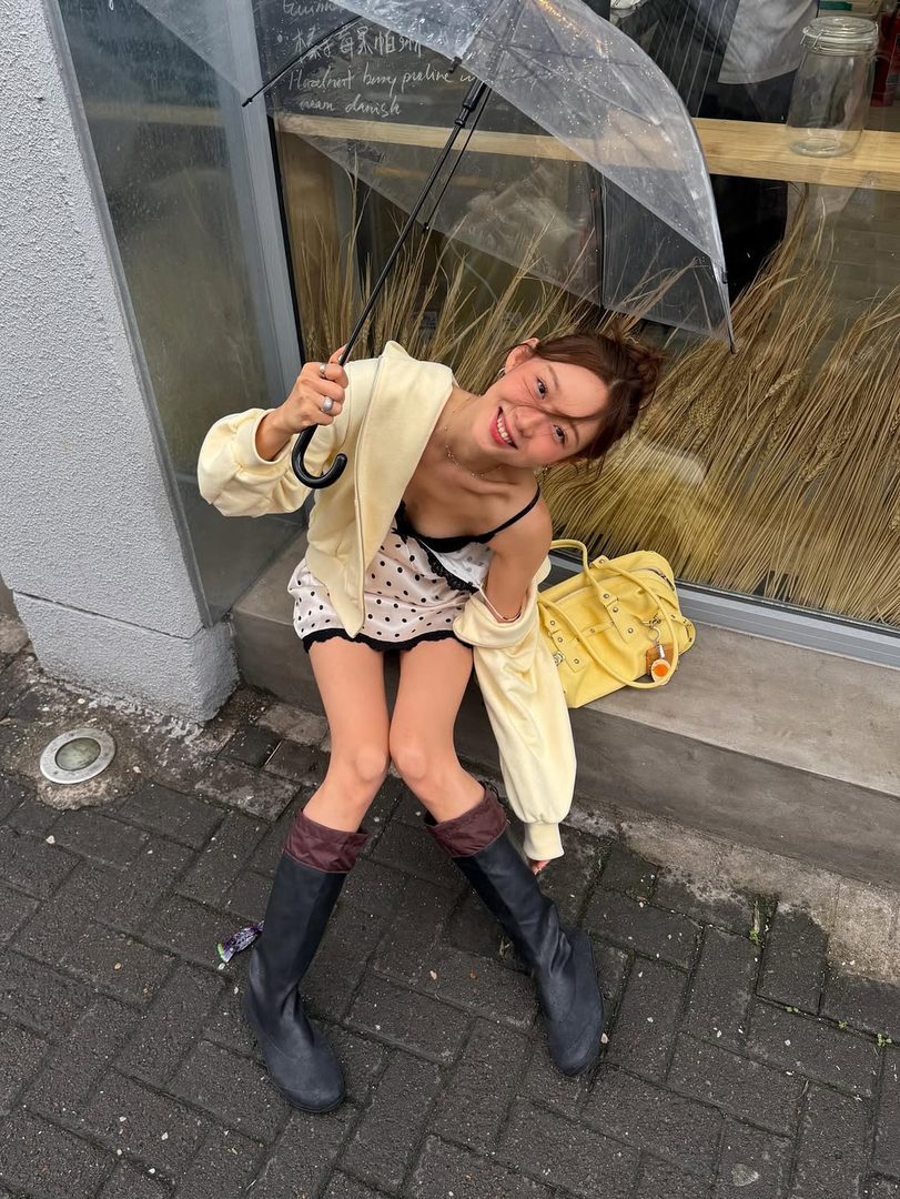 Smiling woman with a clear umbrella and yellow bag on a rainy city street