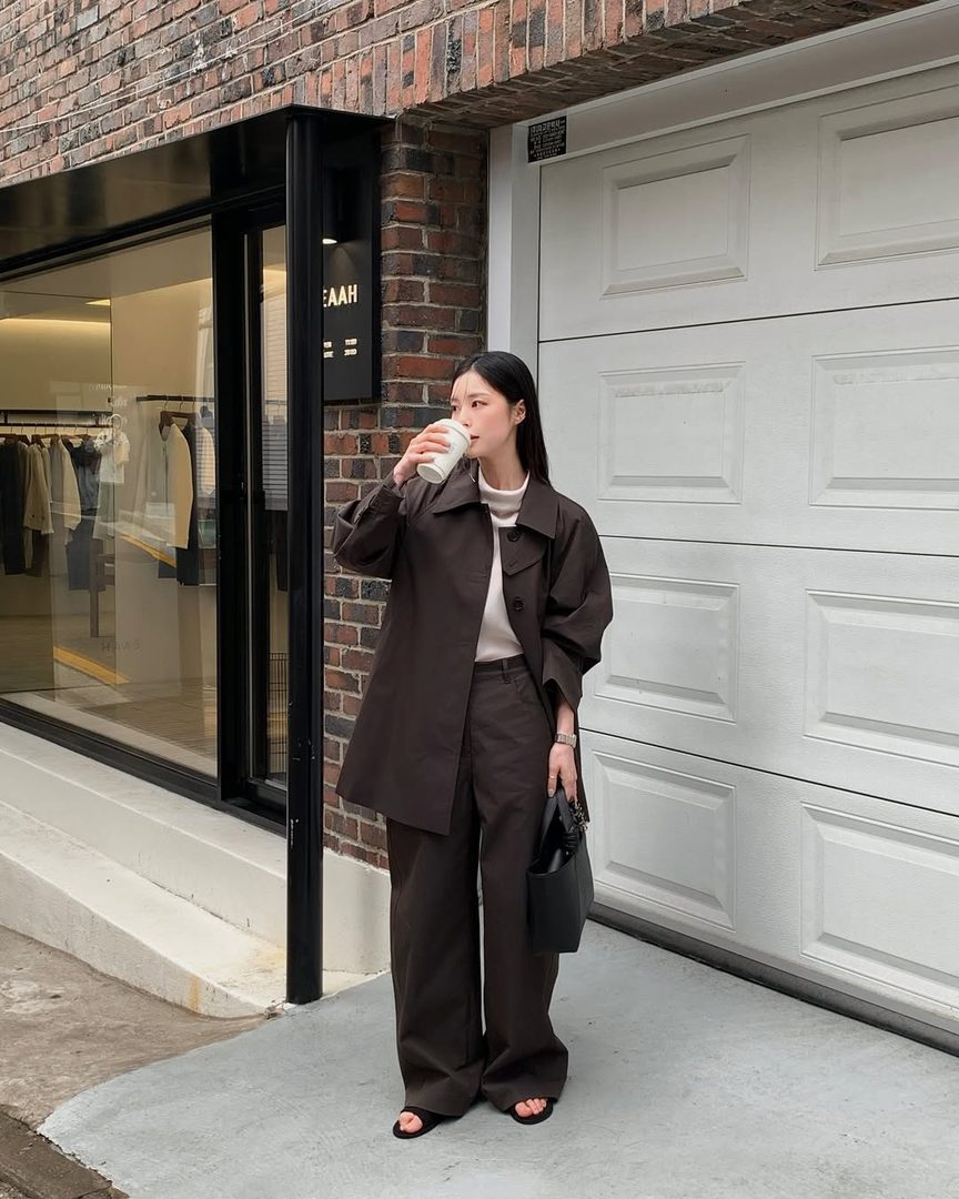 Woman in a dark brown oversized suit drinking coffee outside a boutique