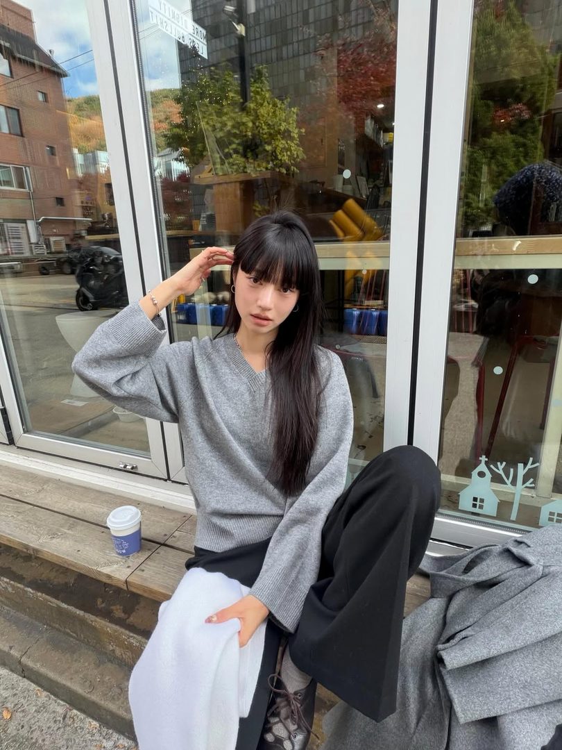 Woman in a grey V-neck sweater sitting outside a café in autumn
