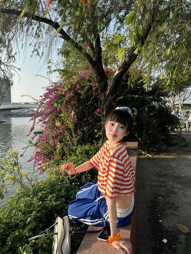Woman in an orange striped shirt by a riverside framed with pink bougainvillea